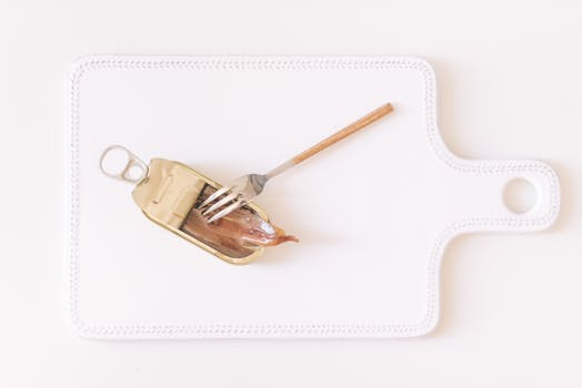 Canned Anchovies and a Fork Lying on a Cutting Board